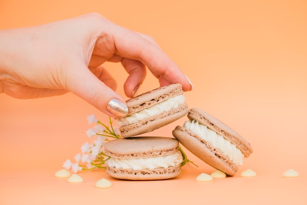 Mão da fêmea com verniz de unha dourada tomando macaroon contra o pano de fundo colorido Foto gratuita
