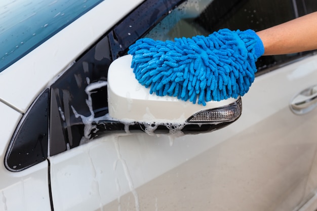 Mão da mulher com a tela azul da microfibra que lava o carro moderno do espelho lateral ou o automóvel da limpeza. Foto Premium