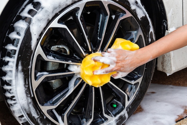 Mão da mulher com o carro moderno da roda de lavagem da esponja amarela ou o automóvel da limpeza. Foto Premium