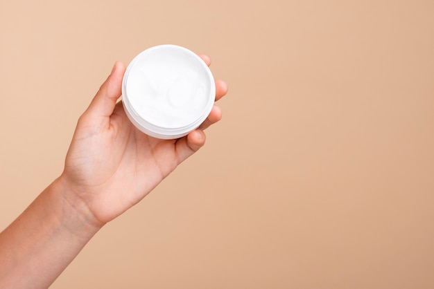 Mão de close-up, segurando o frasco de creme com cópia-espaço Foto gratuita