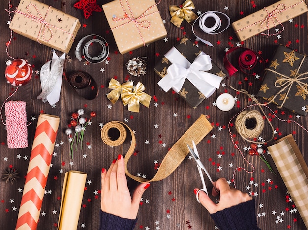 Mão de uma mulher segurando a fita de serapilheira com uma tesoura para cortar e embalar a caixa de presente de natal Foto gratuita