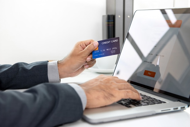 Mão do empresário segurando o cartão de crédito, fazendo o pagamento on-line com o computador portátil Foto Premium