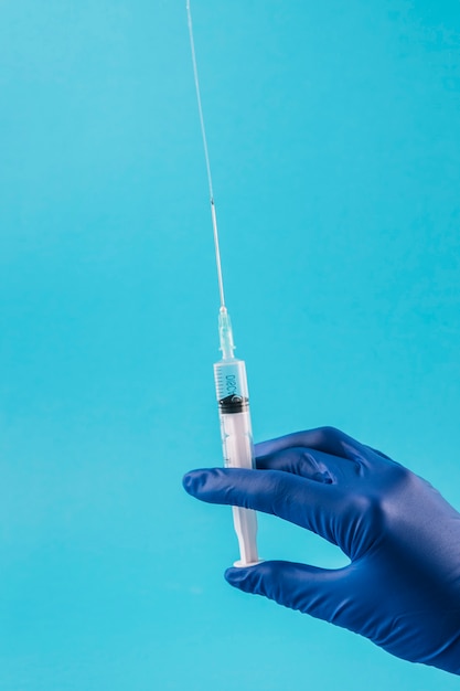 Mão do médico com injeção no pano de fundo azul Foto gratuita
