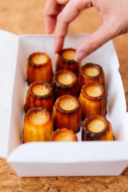 Mão fêmea que escolhe canelés cozido fresco dentro da caixa de papel branco. Foto Premium