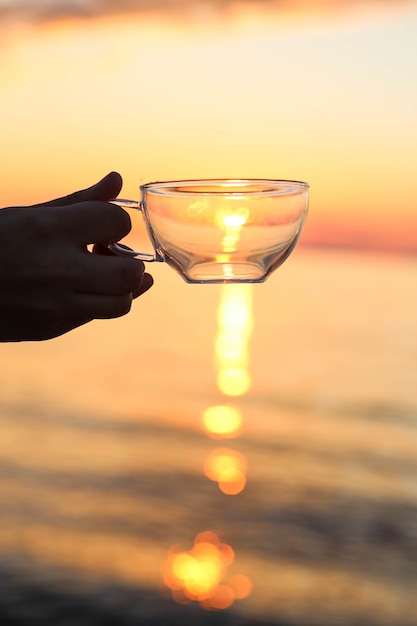 Mão segurando o copo de vidro na frente do pôr do sol | Foto Grátis