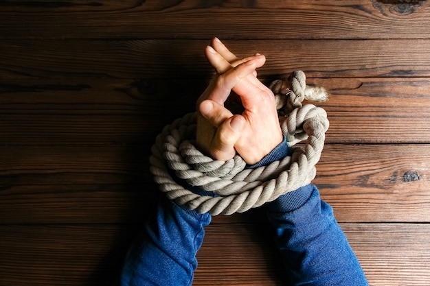 Mãos Amarradas Com Uma Corda Com Risco De Vida Em Um Fundo De Madeira Foto Premium