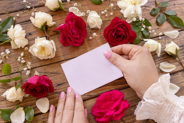 Mãos Com Cartão De Papel Em Branco Cercado Por Rosas Vermelhas E Creme Fecham Sobre Uma Mesa De 0696