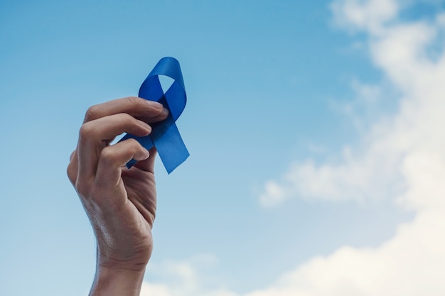 Mãos de homem segurando uma fita azul sobre o céu azul, conscientização do câncer de próstata, novembro azul Foto Premium