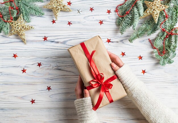 Mãos de mulher segurando embrulhado presente de natal com decoração de estrelas de árvore e sparklins de abeto Foto Premium