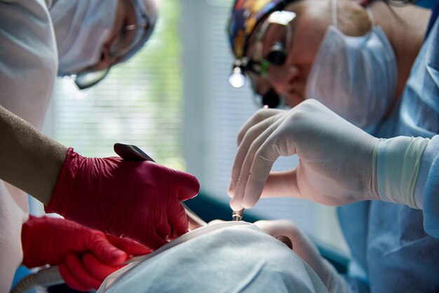 Mos Do Cirurgio Do Dentista E Do Assistente Com O Instrumento Durante