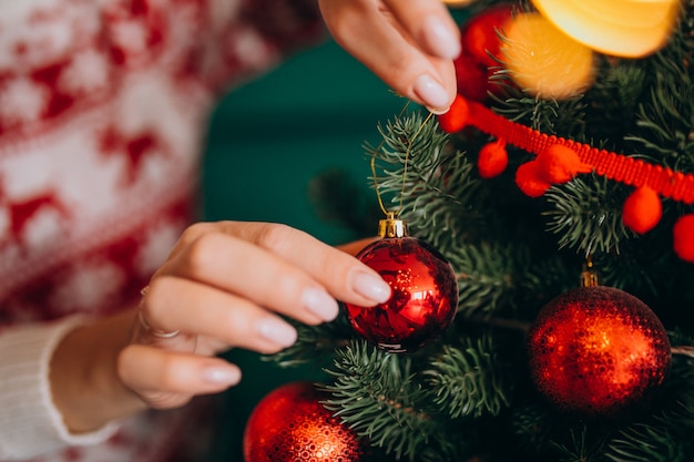 Mãos femininas fechem, decorando a árvore de natal com bolas vermelhas Foto gratuita