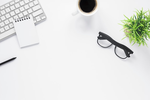 Maquete do espaço de trabalho de escritório em casa com o bloco de notas em espiral; teclado; café; óculos e planta Foto gratuita