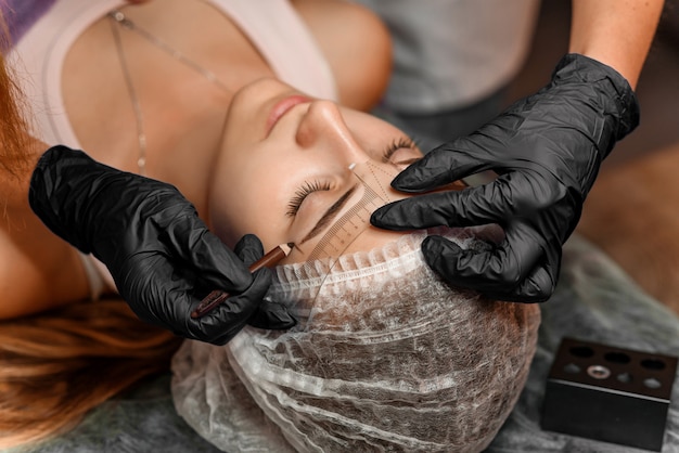 Maquiagem permanente sobrancelha no salão de beleza, closeup. esteticista profissional marca o comprimento das sobrancelhas com lápis e uma régua especial de medição de sobrancelha. tratamento de cosmetologia. Foto Premium