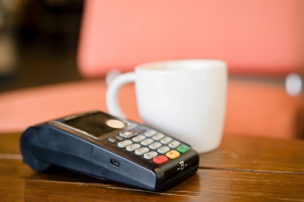 Máquina de pagamento com cartão de crédito com copo de café branco na mesa no café Foto Premium