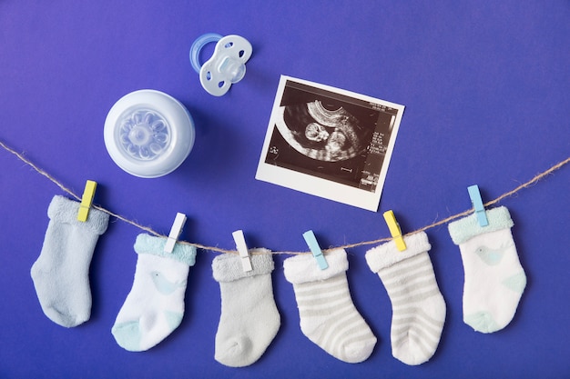Meia do bebê pendurado no varal com garrafa de leite; imagens de chupeta e ultra-som em pano de fundo azul Foto gratuita