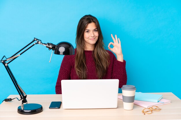 Menina adolescente com um laptop em uma mesa, mostrando um sinal de ok com os dedos Foto Premium