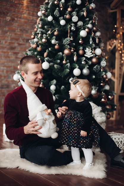 Menina bonitinha sentada com seu pai com árvore de natal Foto Premium