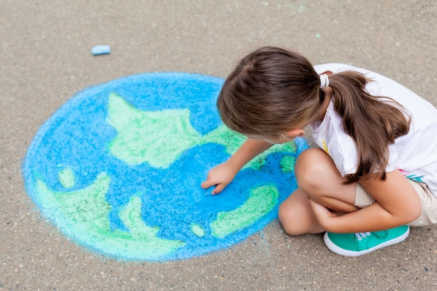 Menina desenhando uma terra globo com giz no asfalto Foto Premium