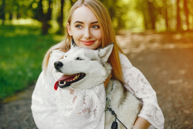 Menina gentil com cabelo claro vestido de branco está jogando junto com seu cachorro Foto gratuita