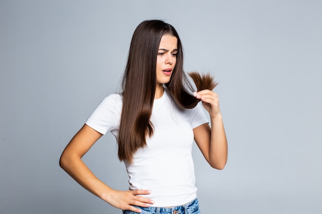 Menina triste, olhando para os cabelos danificados, isolado no branco Foto gratuita