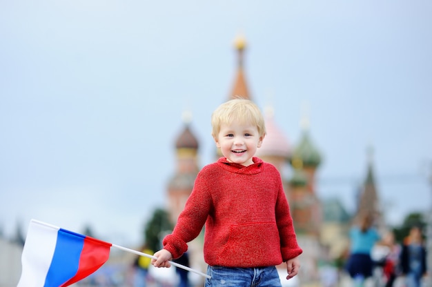 Menino bonito da criança segurando a bandeira russa com a red square e vasilevsky descida Foto Premium