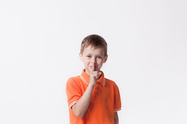 Menino sorridente com o dedo nos lábios, fazendo um gesto silencioso Foto gratuita