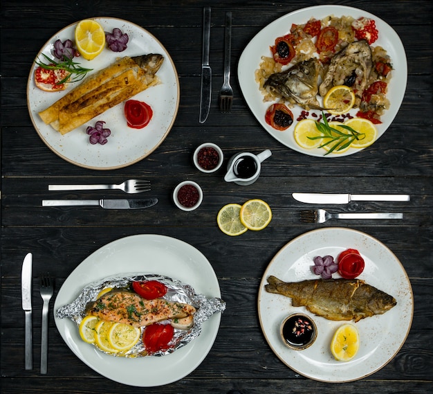 Menu de jantar para 4 pessoas, peixe diferente, frutos do mar em pratos brancos com talheres e molhos Foto gratuita