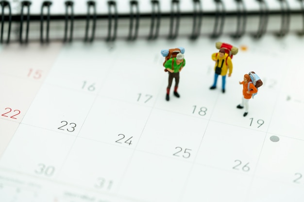 Miniatura de turistas com mochilas de pé no calendário de viagens Foto Premium