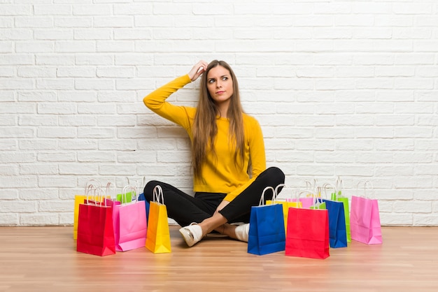 Moça com muitos sacos de compras que têm dúvidas ao coçar a cabeça Foto Premium