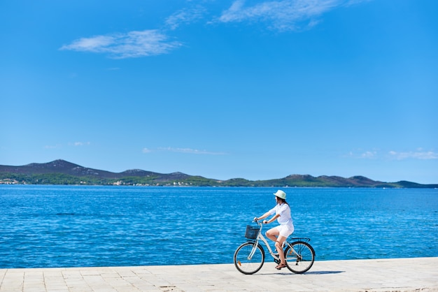 Mulher andando de bicicleta ao longo da calçada pedregosa na água do mar com gás azul Foto Premium