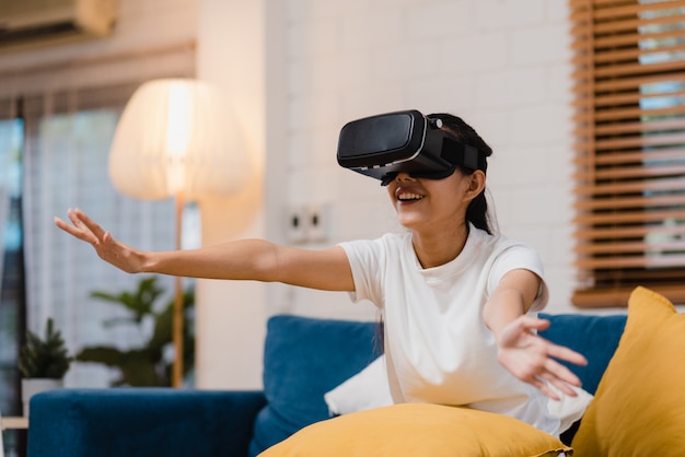 Mulher asiática do adolescente usando óculos simulador de realidade virtual jogando videogame na sala de estar Foto gratuita