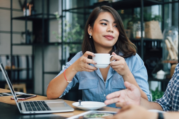 Mulher asiática na camisa azul no café, bebendo café e conversando com o namorado sorriso e cara feliz Foto Premium