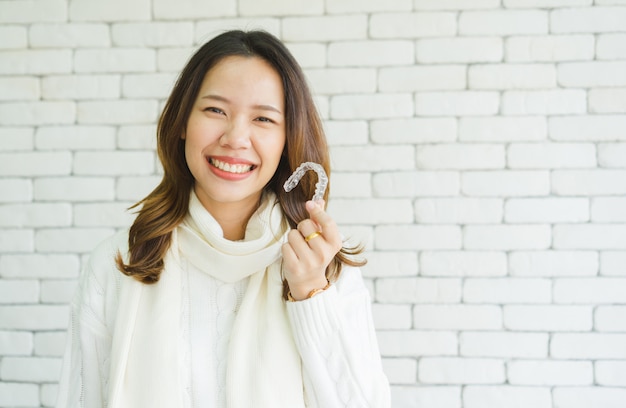 Mulher asiática, sorrindo com a mão segurando o retentor de alinhador dental (invisível) Foto Premium