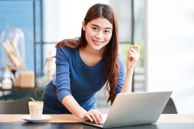 Mulher asiática tomando café e trabalhando com o computador portátil Foto Premium