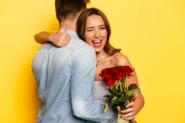 Mulher atrativa com rosas vermelhas que pisc e que mostra um polegar ao abraçar seu noivo. Foto gratuita