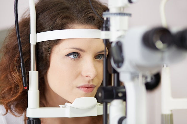 Mulher bonita está olhando para a máquina de teste do olho com concentração no laboratório de oculista Foto Premium