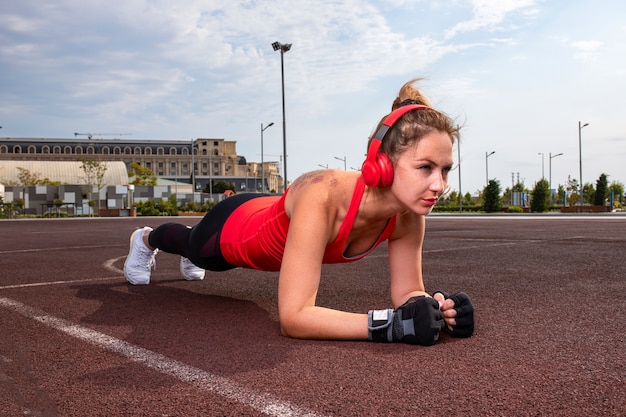 Mulher com fones de ouvido vermelhos e roupas de esporte, fazendo exercícios de ginástica. Foto gratuita