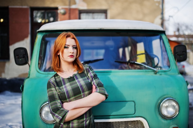 Mulher de cabelo vermelha nova que levanta no vestido quadriculado na carrinha ciana retro velha. Foto Premium