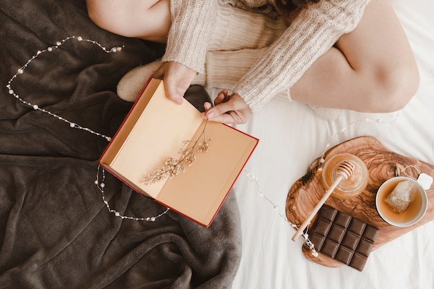 Mulher de colheita com livro perto de chá e doces Foto gratuita