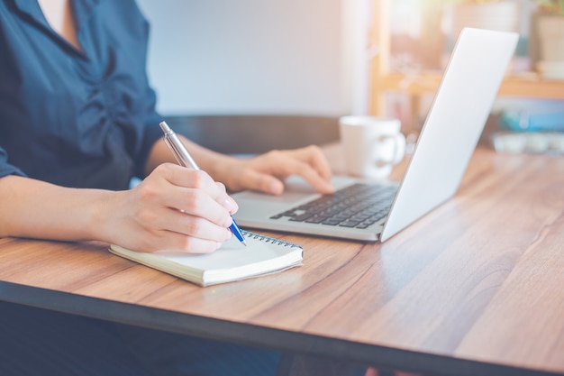 Mulher De Negócios Está Escrevendo Em Um Caderno Com Uma Caneta E Usando Um Laptop Para 8736