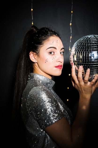 Mulher encantadora com brilhos no rosto segurando bola de discoteca Foto gratuita