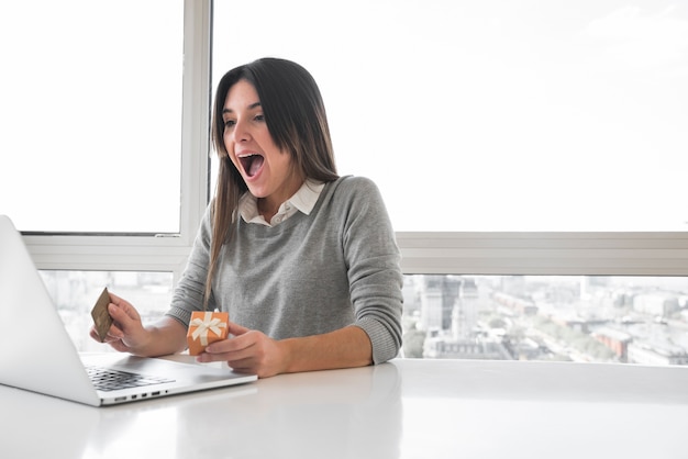 Mulher espantada, sentado à mesa com o laptop Foto gratuita