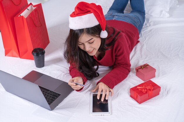 Mulher feliz compras on-line para presente de natal com tablet digital e cartão de crédito na cama Foto Premium