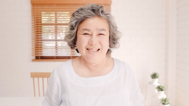 Mulher idosa asiática que sente feliz sorrindo e olhando à câmera quando relaxe no sofá na sala de visitas em casa. conceito superior das mulheres do estilo de vida em casa. Foto gratuita