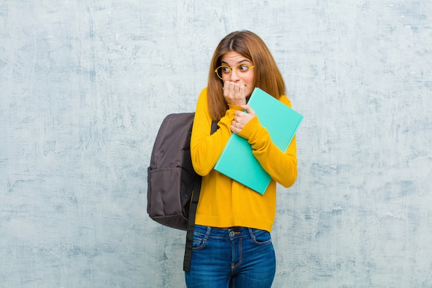Mulher jovem estudante olhando preocupado, ansioso, estressado e com medo, roer unhas e olhando para o espaço da cópia lateral contra a parede da parede do grunge Foto Premium