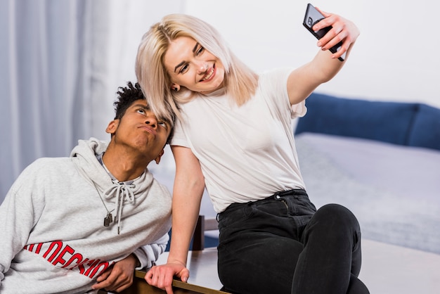 Mulher jovem sorridente tomando selfie no celular com o namorado fazendo careta Foto gratuita