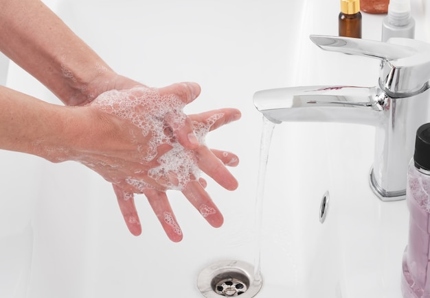 Mulher lava as mãos com sabonete embaixo da torneira do banheiro Foto gratuita