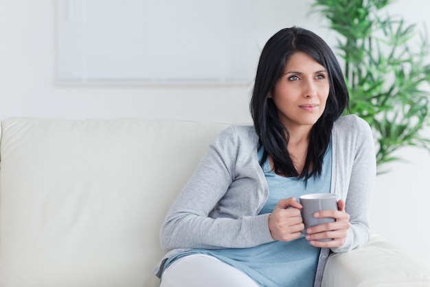 Mulher Pensativa Sentada Em Um Sof Enquanto Segura Uma Caneca Foto