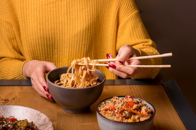 Mulher segurando os pauzinhos com macarrão na mesa Foto gratuita