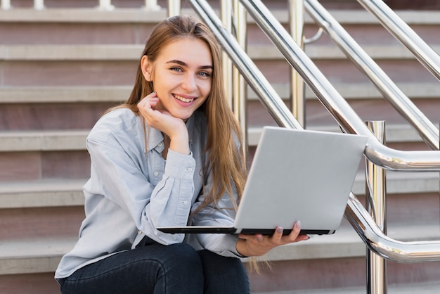 Mulher Sorridente Sentado Na Escada E Segurando Um Laptop Foto Grtis